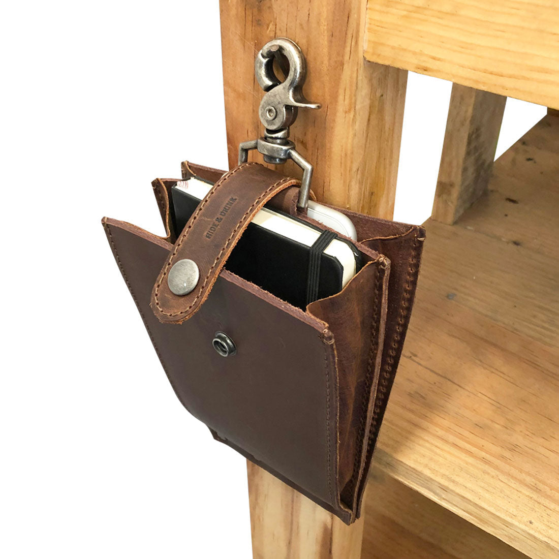 The 'Table Hanger Organizer' by Hide & Drink hanging from a wooden shelf, showcasing its functionality and stylish design in full grain leather—perfect for any setting. Table Hanger Organizer - All-Purpose Slim File with Lobster Clasp - Durable Multi Use Hanger Organizer with Clasp, Full Grain Leather, StockyardX, Small Batch Production, Hand Cut, Hand Sewn, Fire Branded, Artisan, Handmade in La Antigua Guatemala & Oaxaca Mexico.