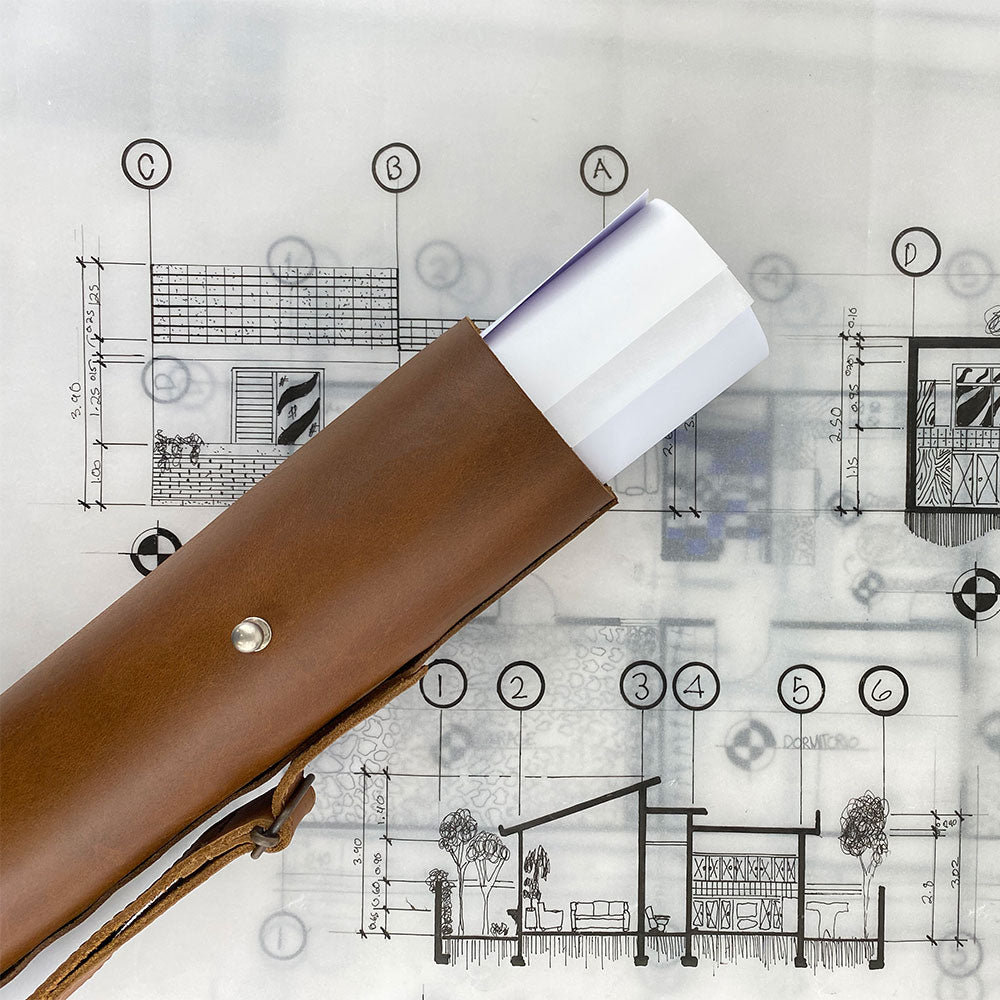 Hide & Drink's Blueprint Tube (A2 Paper Size) displayed with accompanying brand card. This full grain leather tube includes an adjustable strap for easy transport. Perfect for storing architectural documents, it's a testament to handmade quality and artisan craftsmanship from StockyardX in La Antigua Guatemala & Oaxaca Mexico.