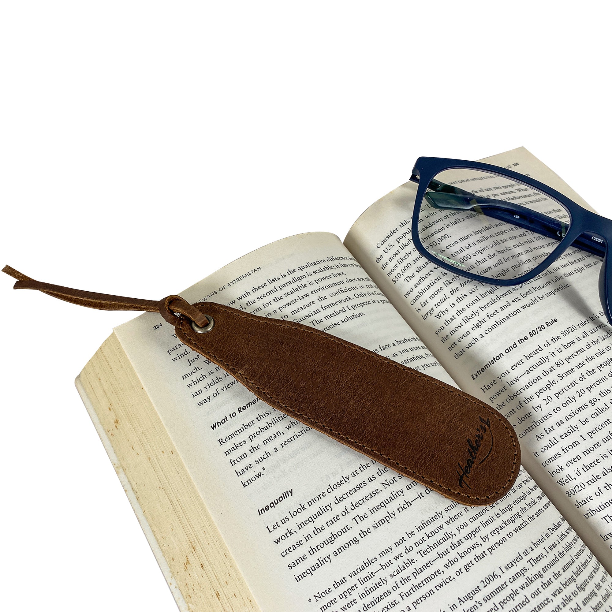 Heather's Bookmark (3 Pack) with a full grain leather bookmark resting on an open book next to glasses. A perfect fusion of practicality and elegance for book lovers. Bookmark Page Marker (3 Pack) Book Lovers, Page Turners, Travel Readers, Literature Fans, Book Club Gifts, Full Grain Leather, StockyardX, Small Batch Production, Hand Cut, Hand Sewn, Fire Branded, Artisan, Handmade in La Antigua Guatemala & Oaxaca Mexico.