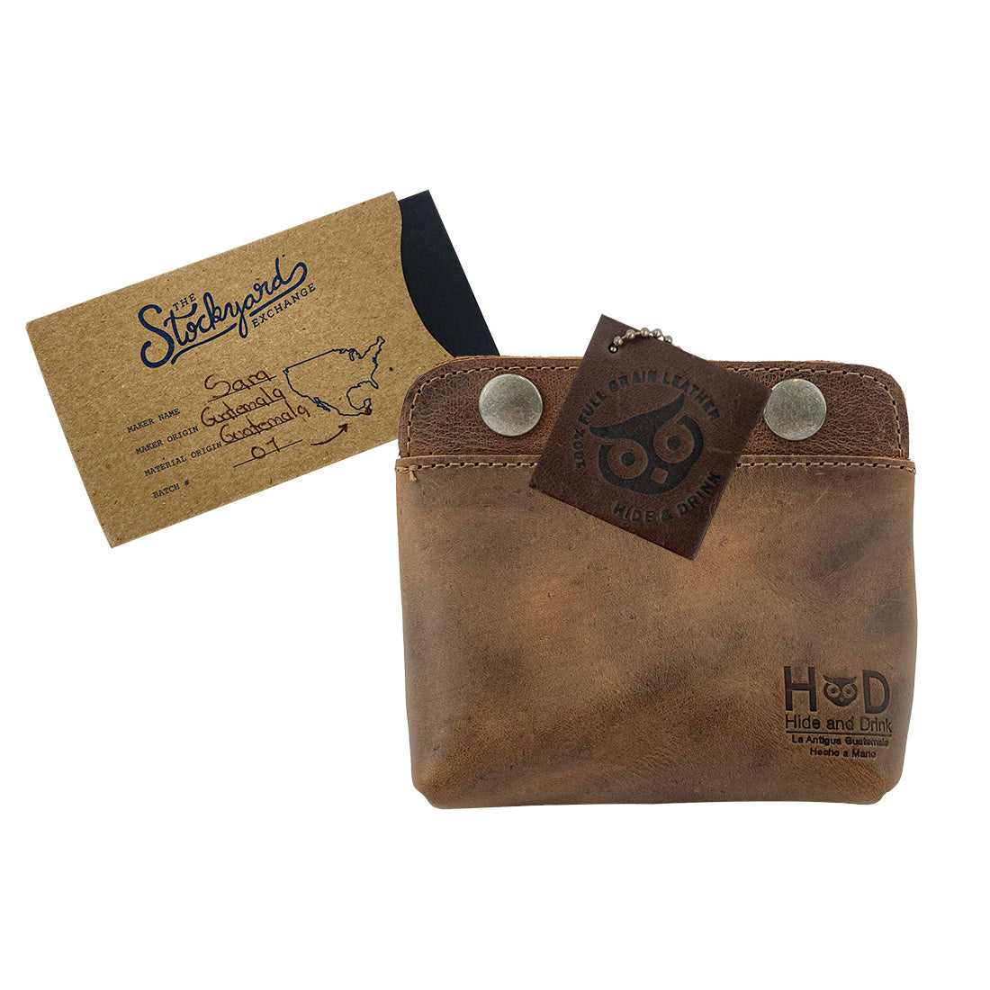 Hide & Drink's Double Snap Pouch displaying the tag that tells its story, showcasing its function as a coin purse, cash & card holder, and a makeup organizer. This full grain leather piece is artisan handmade in La Antigua Guatemala.