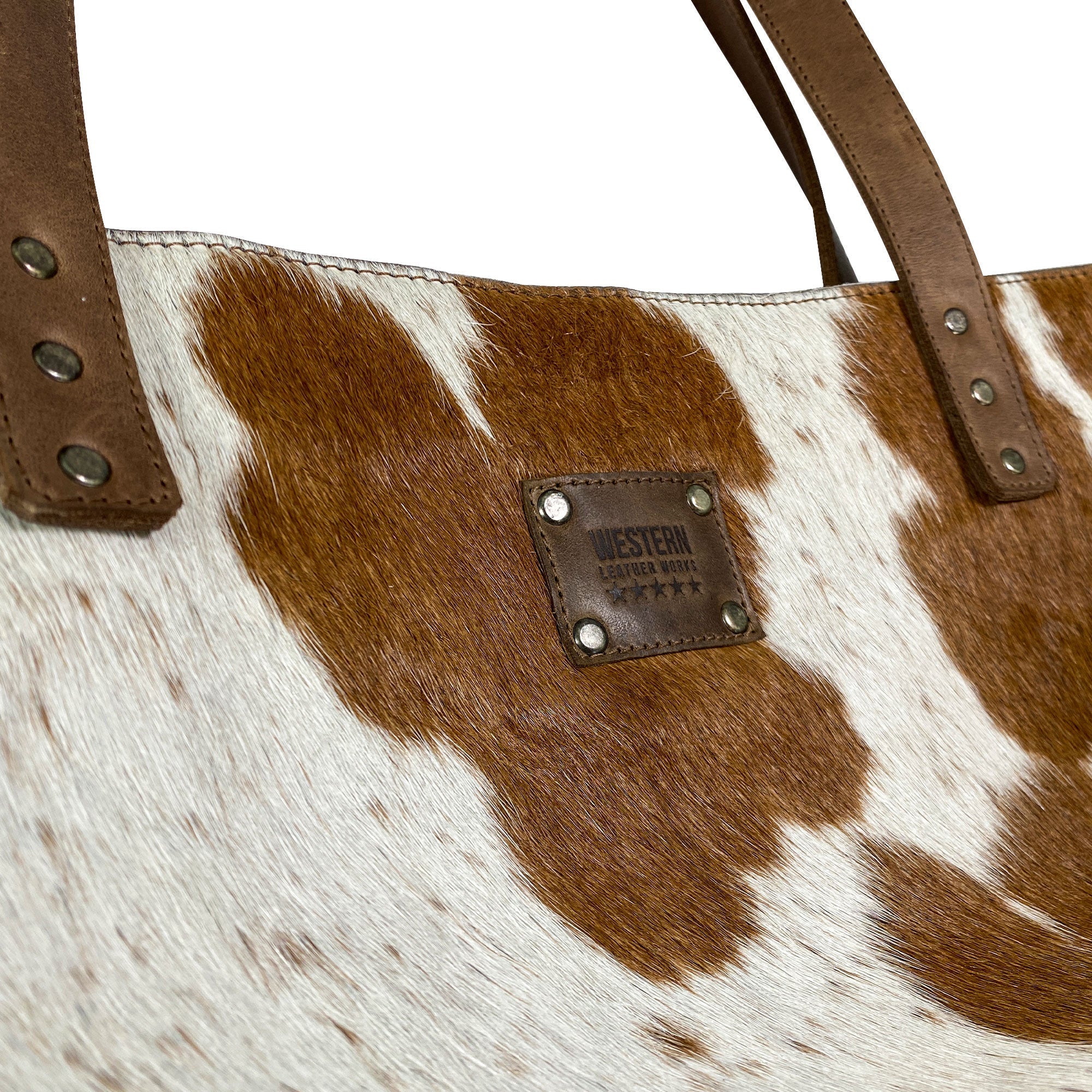 Close-up of the Western Leather Works Formal Tote Bag highlighting the distinctive Hair on Hide Full Grain Leather texture and fire branded label. This unique design adds charm to the spacious tote, ideal for everyday wear. Handmade with care, featuring a plaid cotton interior lining. Artisan, handmade in La Antigua Guatemala & Oaxaca Mexico.