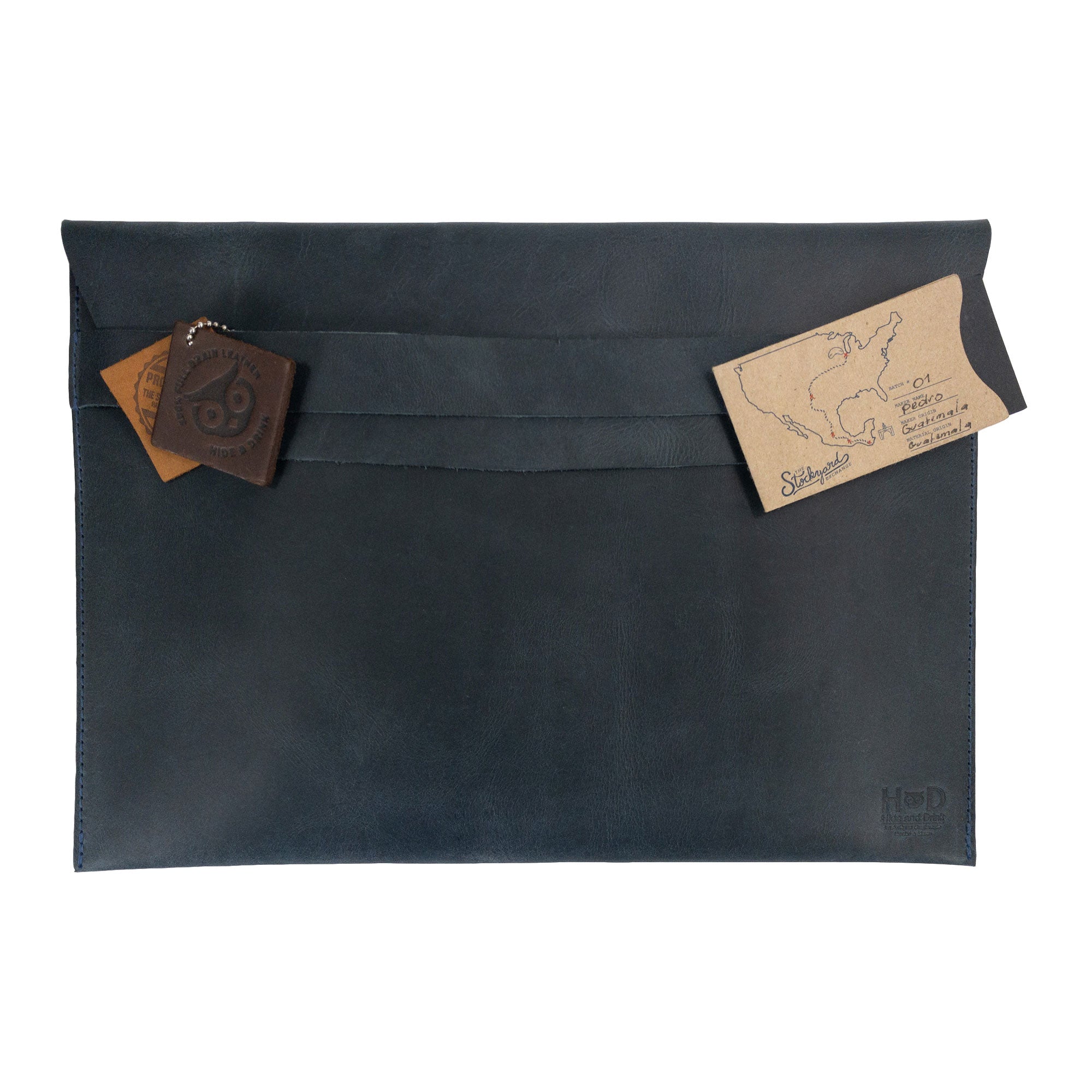 The black Hide & Drink MacBook Slim Case adorned with a decorative leather tag, emphasizing its handcrafted nature. Designed for MacBook Air/Pro 13 Inch with M1 Chip, this case combines rustic aesthetics with artisan quality.
