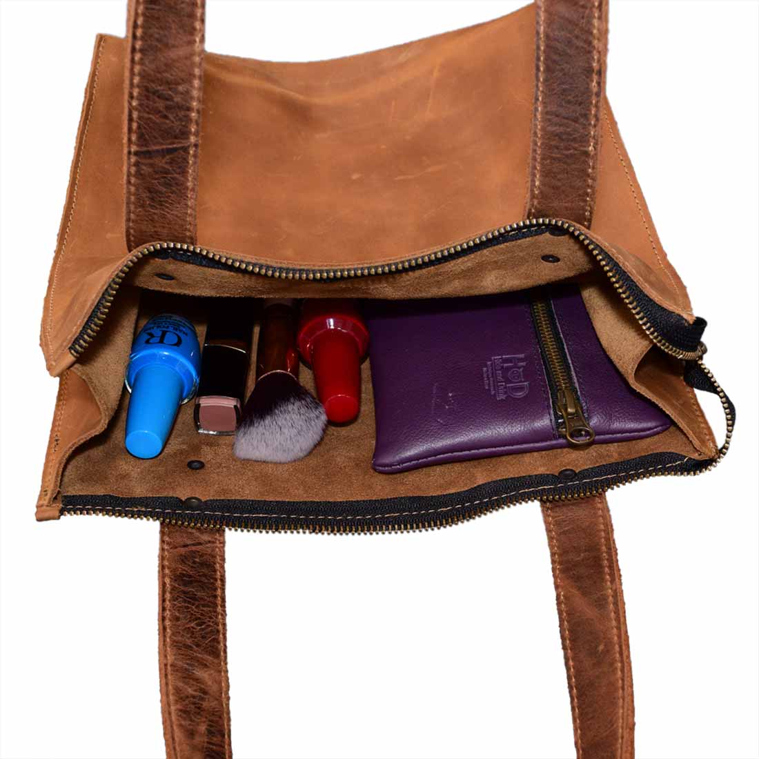 Inside view of the Square Shoulder Bag by Hide & Drink, featuring essential cosmetics and personal items perfectly organized. This handbag is made from premium full grain leather, making it a stylish accessory that blends functionality with vintage charm, reflecting small batch production and artisan craftsmanship from La Antigua Guatemala & Oaxaca Mexico.