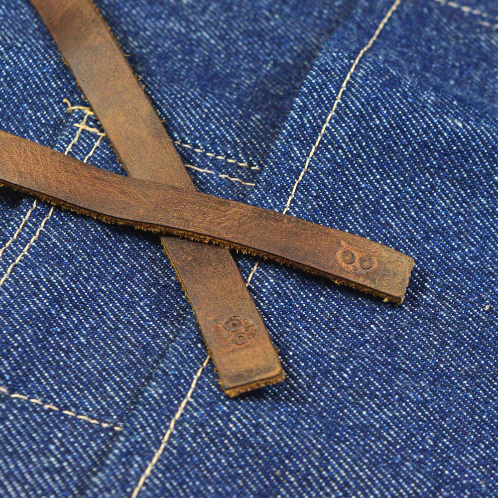 Detail of the leather straps on Hide & Drink's Repurposed Denim Waist Apron, showing the hand cut and rustic finish. This waist apron combines functionality and style, handmade in La Antigua Guatemala & Oaxaca Mexico, with small batch production and fire branded artisan quality.