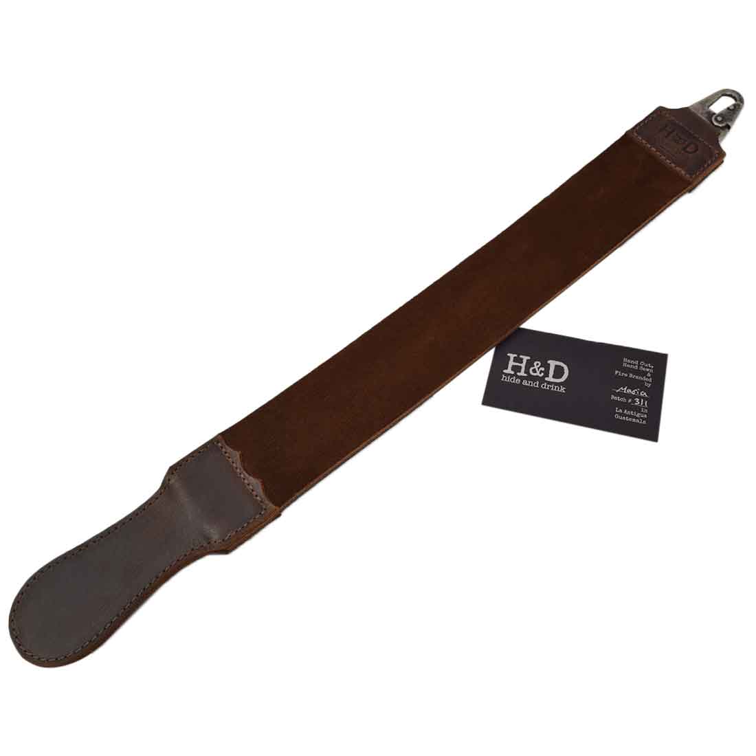 Hide & Drink's Barber Strop laid out with a business card, showcasing the heritage behind its handmade craftsmanship. This Full Grain Leather Razor Strop serves both as a Shaving Sharpener and Barber Straight Razor Strap Belt.