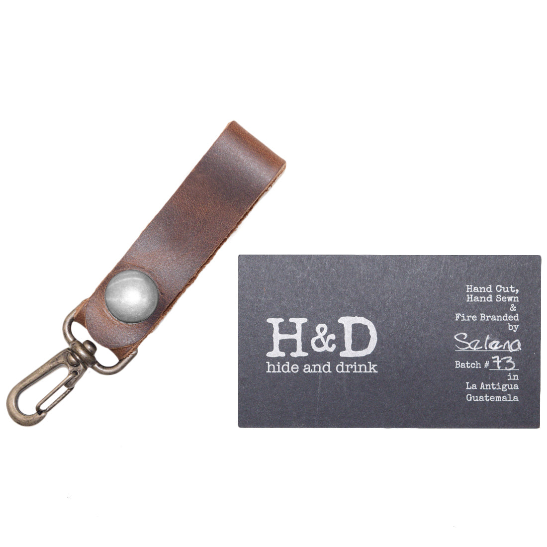 Belt Key Holder by Hide & Drink with a business card, illustrating its handcrafted quality and unique design. Dimensions Length: 4.25 in. Height: 1 in. Width: 0.50 in. Made from Full Grain Leather, it develops a unique patina over time and is best cared for with mineral oil or beeswax.