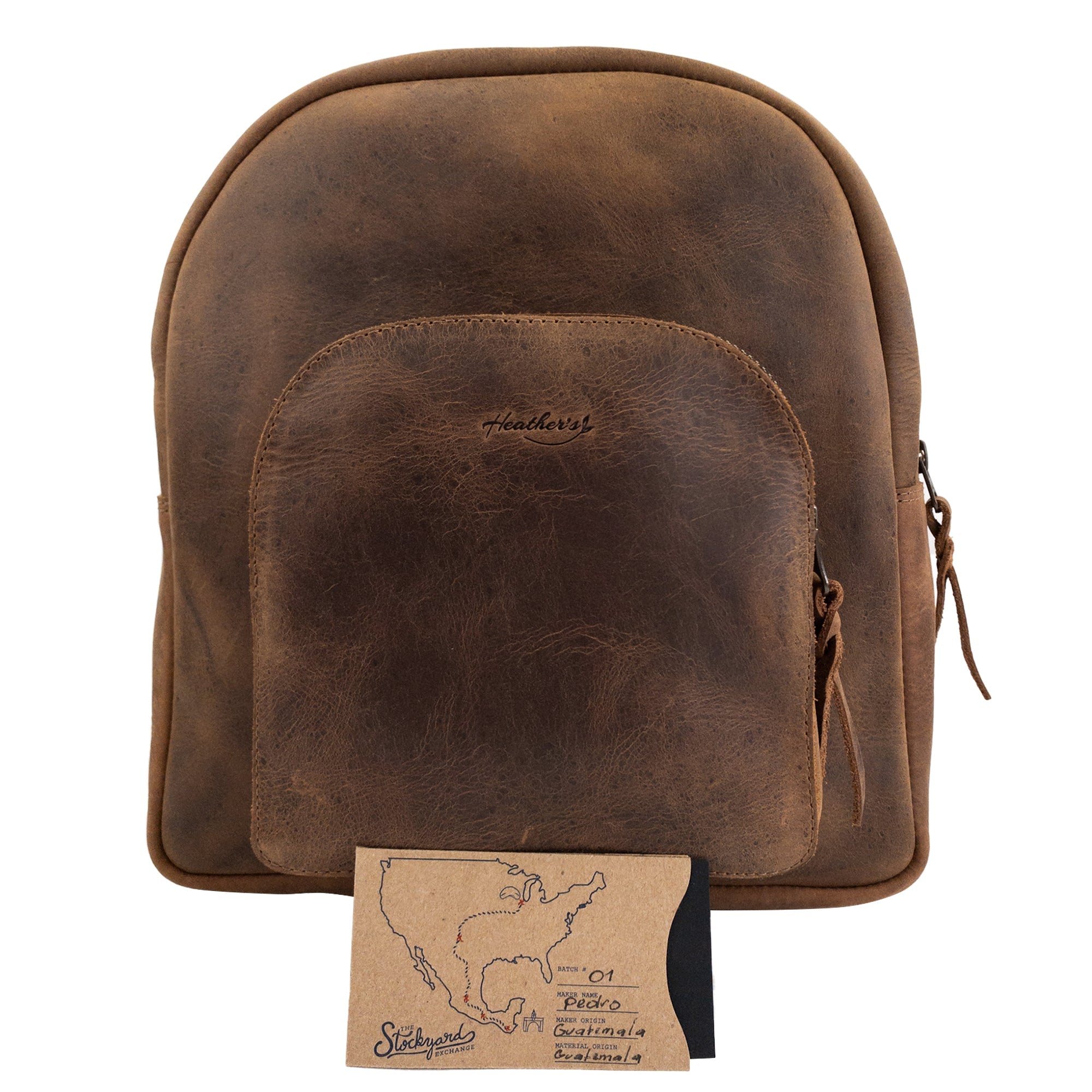 Heather's Minimalist Backpack alongside a tag noting its origin, made from full grain leather. This durable and stylish backpack showcases exquisite craftsmanship and is designed for carrying and organizing essentials like phones and notebooks. Truly an artisan piece, it highlights the importance of small batch production from La Antigua Guatemala.