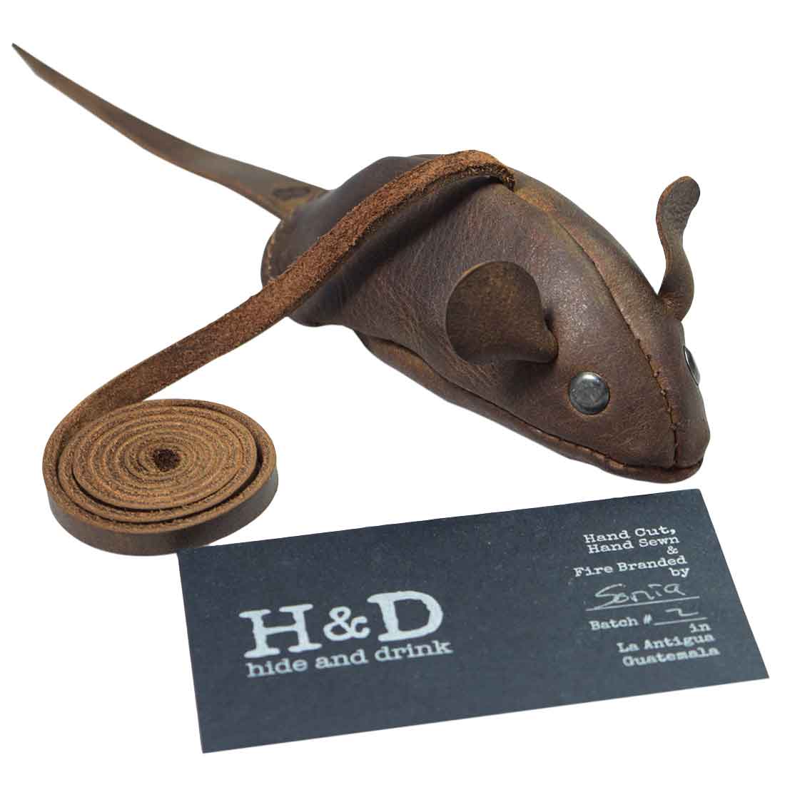 Hide & Drink's Cat Toy displayed alongside its branding card, highlighting craftsmanship. This furry mouse is a fun Cat Teaser made from full grain leather, perfect for engaging your cat. Artisan-made in La Antigua Guatemala, this unique Cats Exerciser Toy showcases dedication to handmade quality through small batch production and careful fire branding.