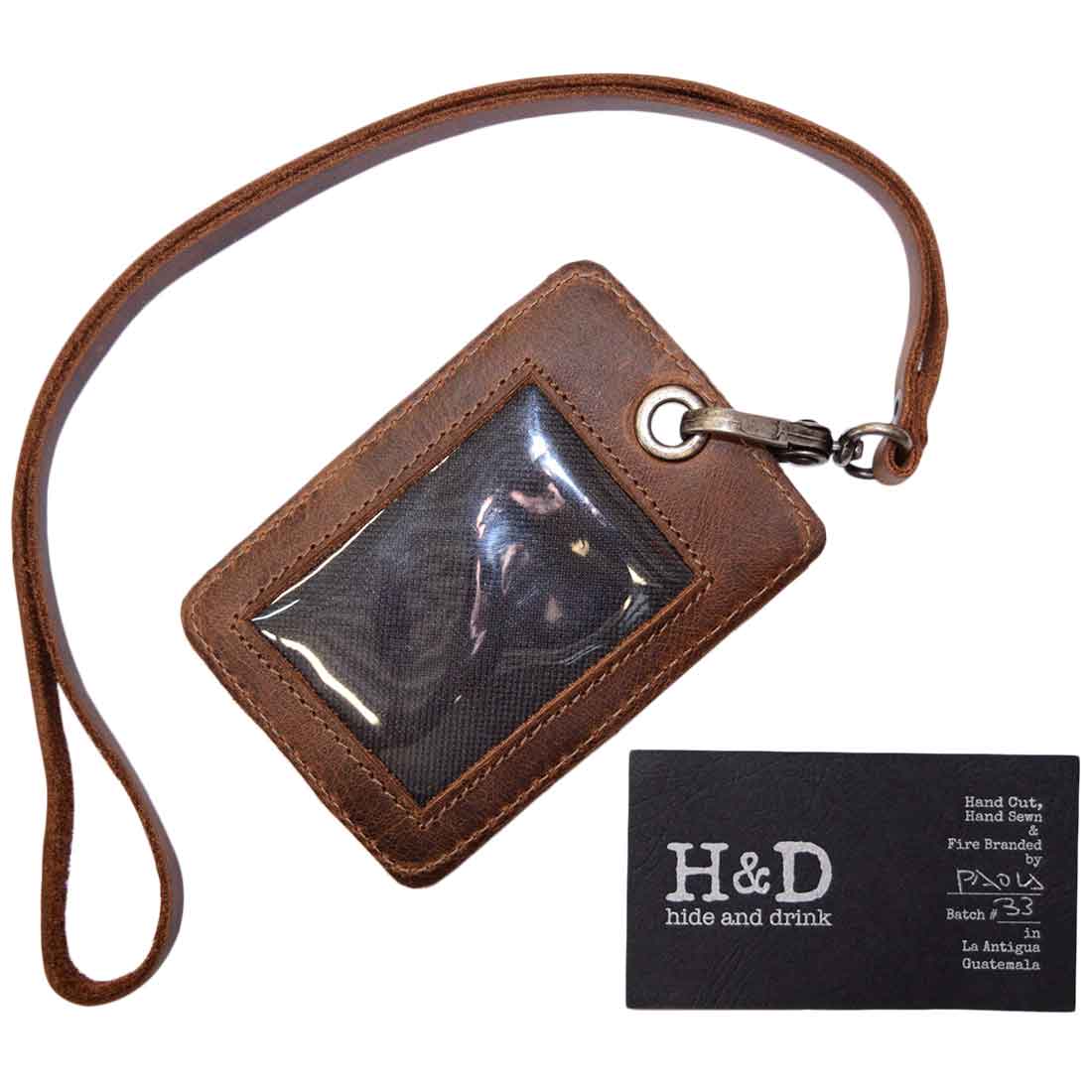 Hide & Drink’s Vertical ID Holder displayed with a business card, showcasing its clear window. Made from durable full grain leather, this artisan piece includes a detachable neck lanyard and is perfect for work accessories, representing small batch production quality.